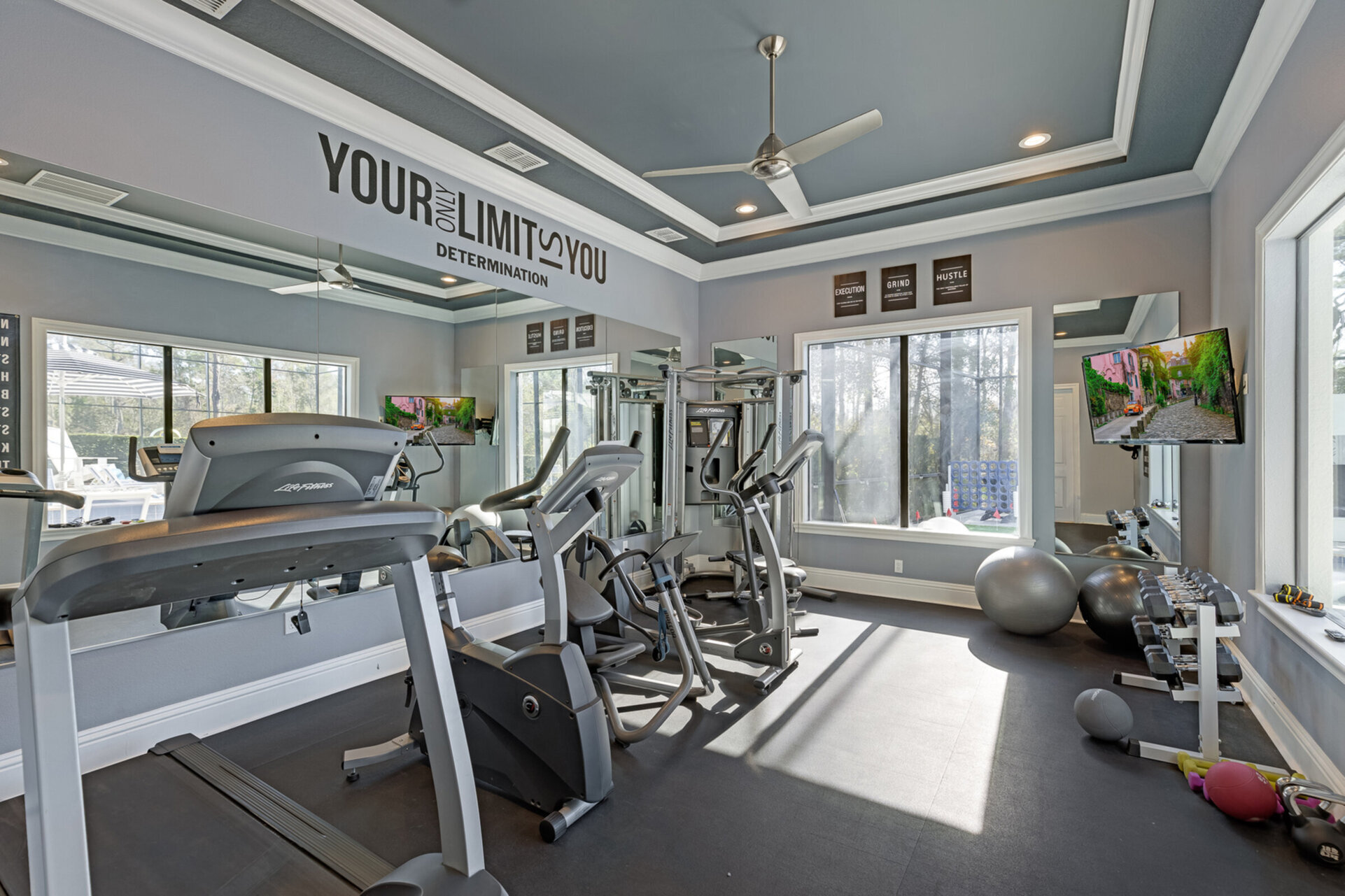 A fitness room with G7 home gym, treadmill, elliptical, bike, free weights and pool views